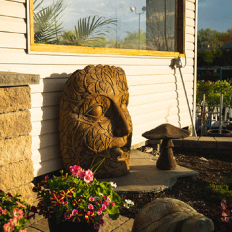A large mask style statue located under a window of a home.